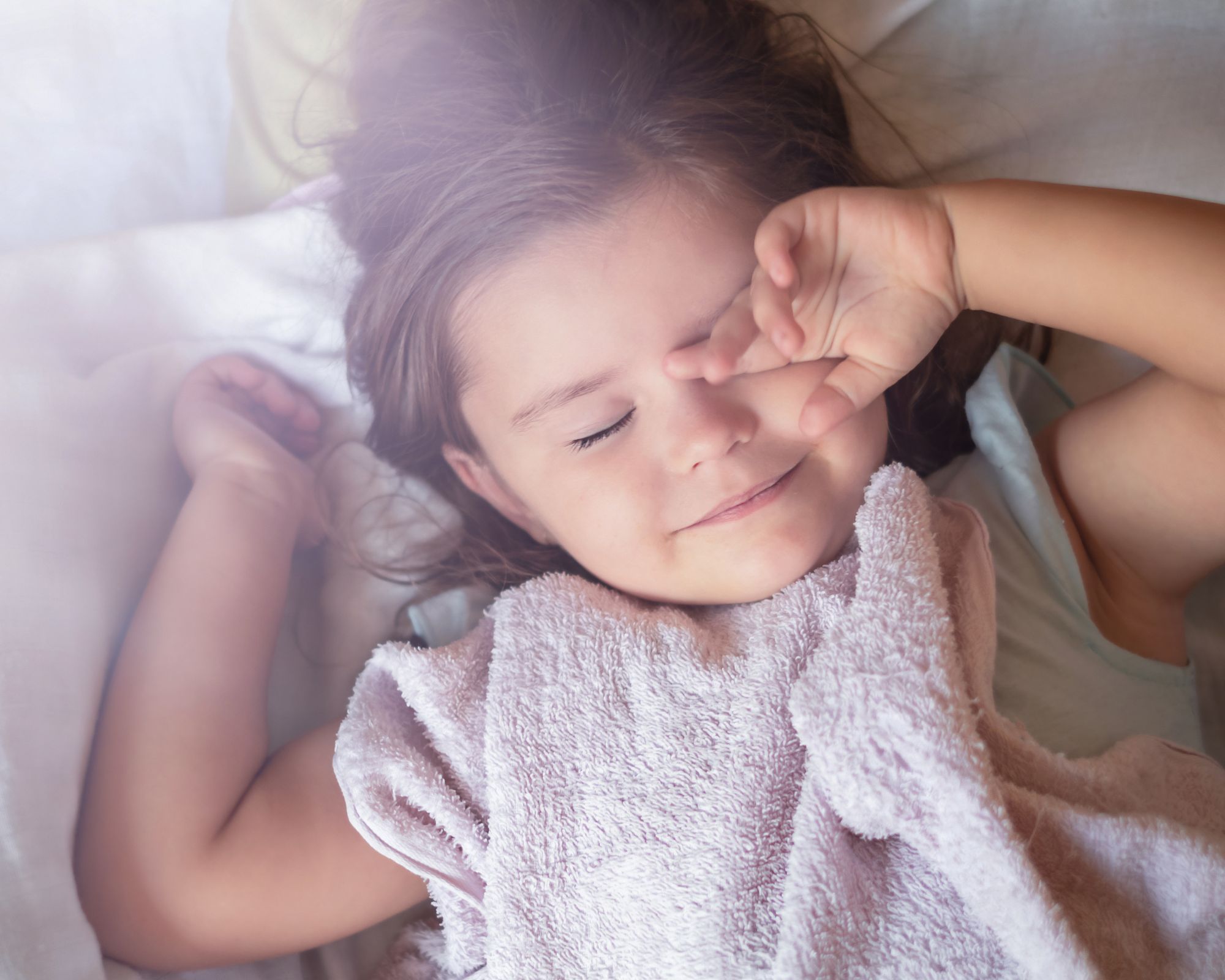 Mädchen liegt im Bett und reibt sich die Augen