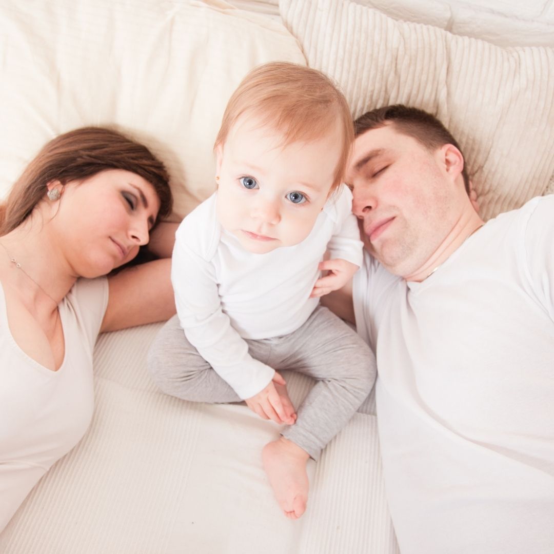 Fruehaufsteher: Mama und Papa schlafen, aber das Kind sitzt wach in der Mitte