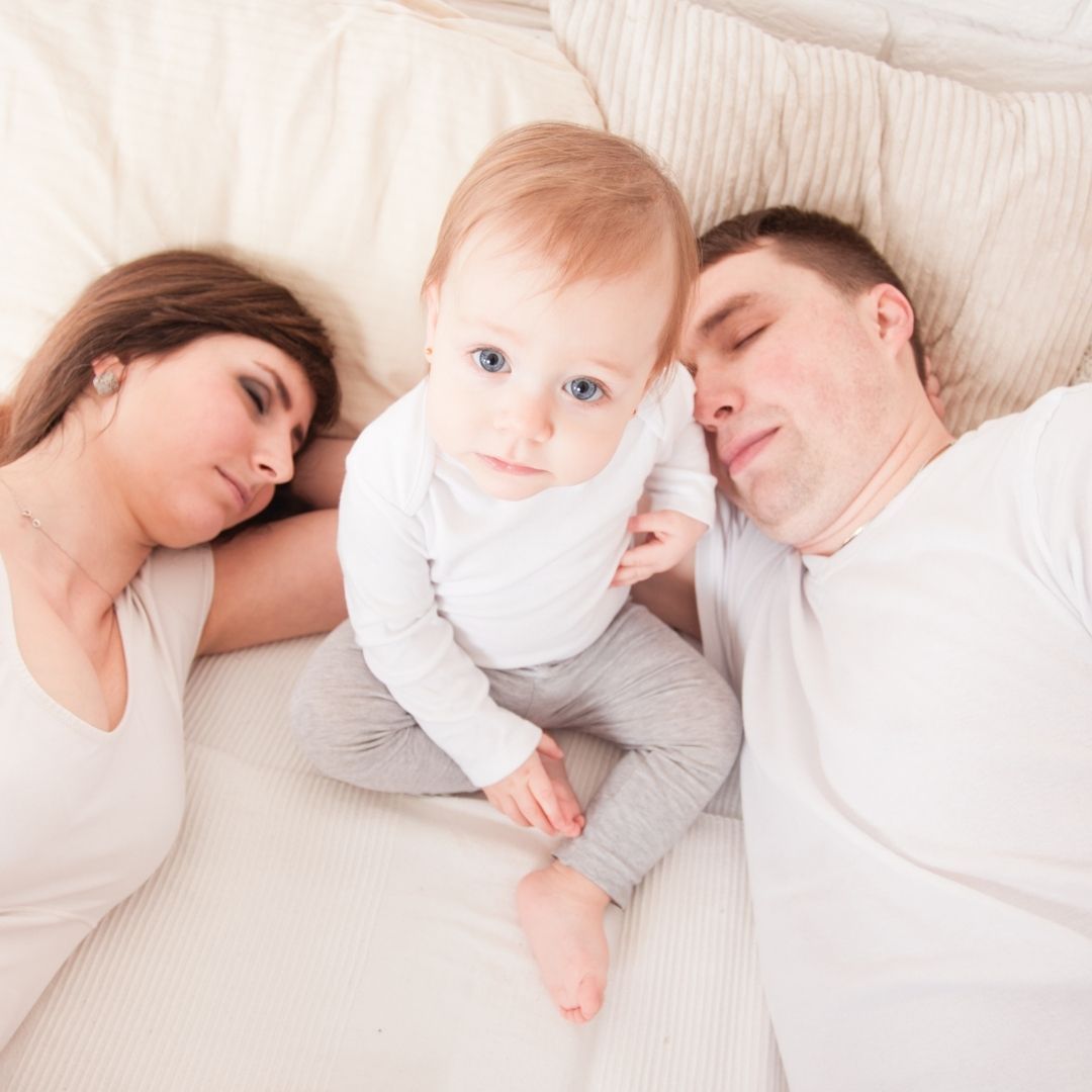 Mama und Papa schlafen und das Baby zwischen ihnen ist wach