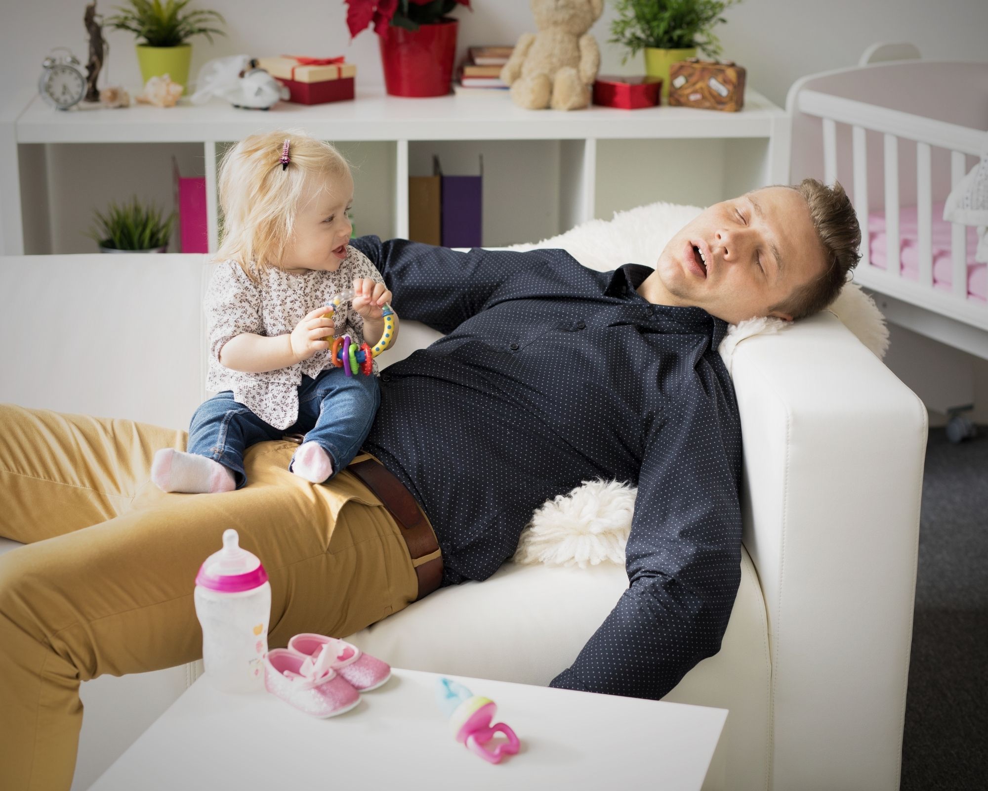 Vater schläft auf der Couch und sein Kind sitzt wach auf ihm