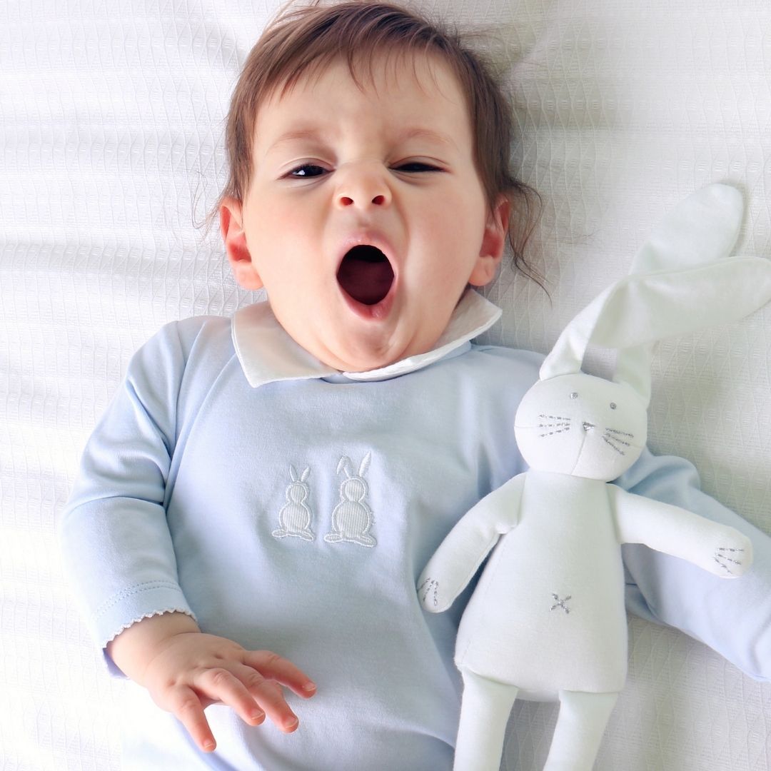 Baby liegt mit Kuscheltier im Bett und gähnt